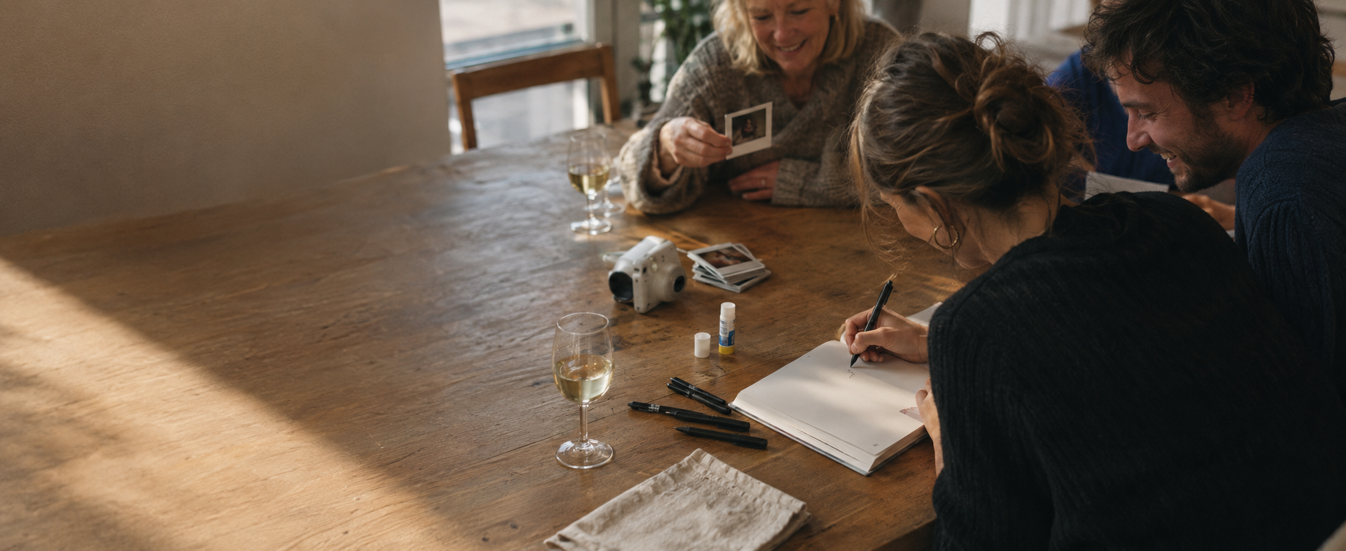 MEMENTO Gästebuch – drei Gäste am Tisch beim Eintragen, mit Sofortbildkamera und Polaroids